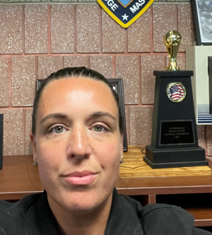 A person with tan skin and dark hair pulled into a ponytail smiles slightly at the camera.