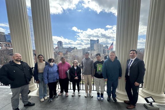 Group of nine adults smiling outdoors at the State House