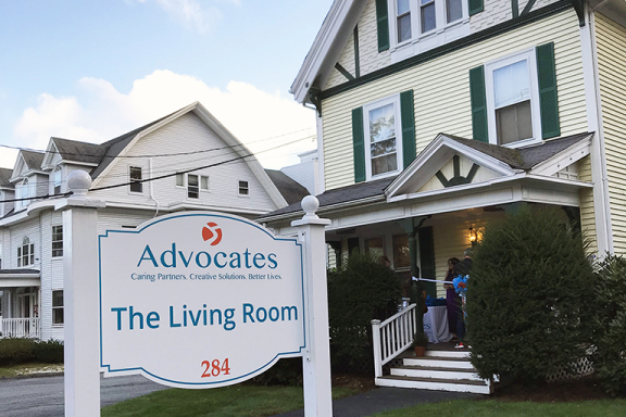 Exterior shot of The Living Room, a yellow house. A sign in the yard says "Advocates The Living Room. 284 Union Avenue."