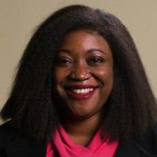 An adult with shoulder length dark hair and brown skin smiles at the camera