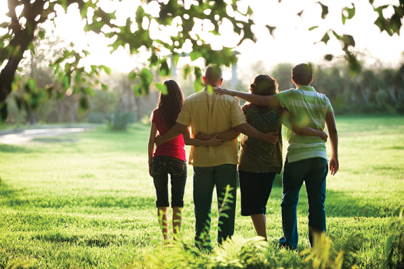 Back view of a group of four people standing with their arms around each other