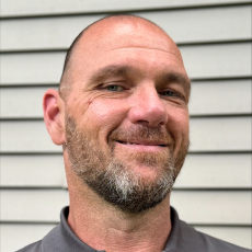 A bald light-skinned adult with a salt and pepper goatee smiles at the camera