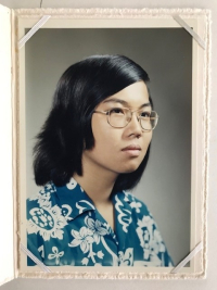 A headshot in profile of a young Asian adult with shoulder-length hair and glasses