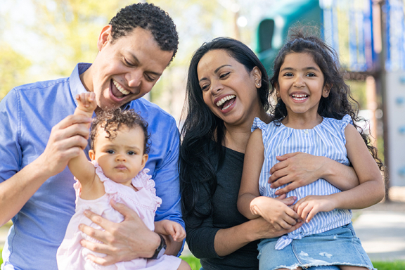 Parents and two young children smiling outside.