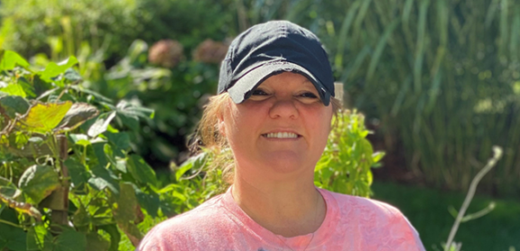 Amanda St. Amant smiling outside. She is wearing a hat and tie dye t-shirt.
