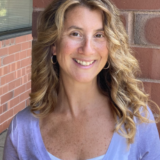 A light-skinned person with long wavy light brown hair smiles at the camera.