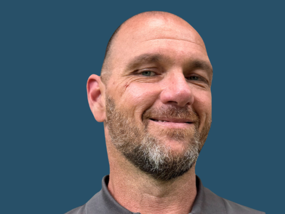 Bald adult with salt and pepper goatee smiles at camera