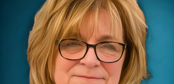 A middle-aged, light skinned woman with honey blond hair and glasses