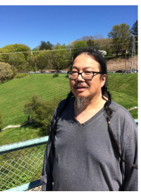 A middle-aged Asian adult with glasses and long braids poses outdoors